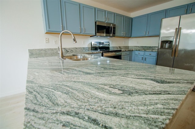 kitchen with light wood-type flooring, stone countertops, appliances with stainless steel finishes, and sink