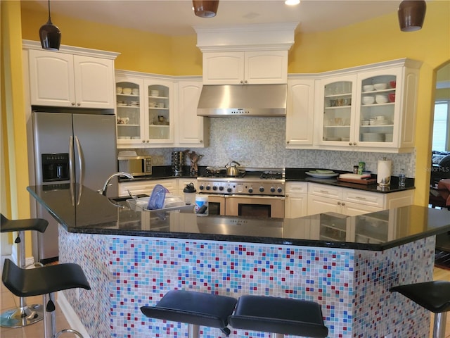 kitchen with a kitchen breakfast bar, tasteful backsplash, white cabinets, and appliances with stainless steel finishes