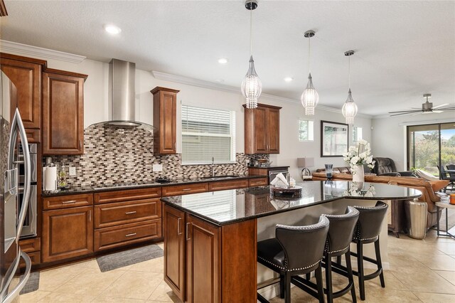 kitchen featuring ceiling fan, a kitchen bar, wall chimney exhaust hood, decorative light fixtures, and a center island