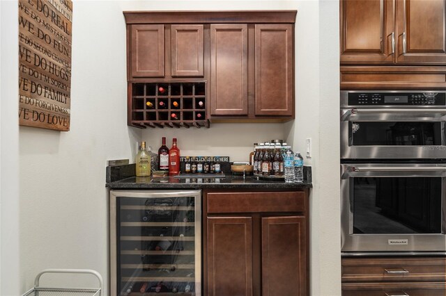 bar with dark stone counters, beverage cooler, and double oven