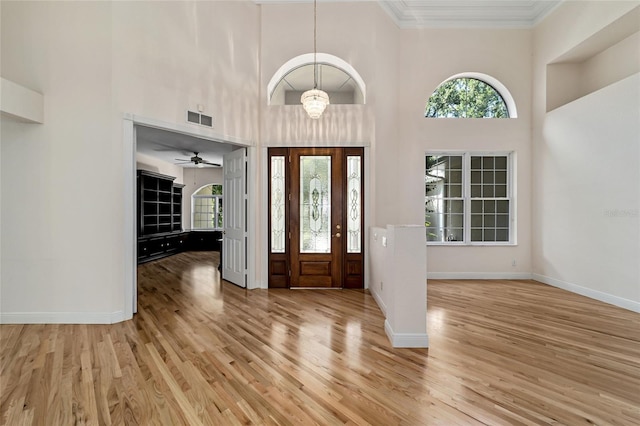 entrance foyer featuring ceiling fan with notable chandelier, ornamental molding, a high ceiling, and light hardwood / wood-style floors