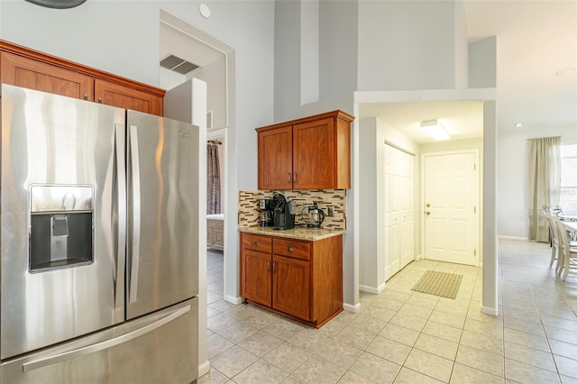 kitchen with a high ceiling, stainless steel fridge, light tile floors, light stone counters, and tasteful backsplash