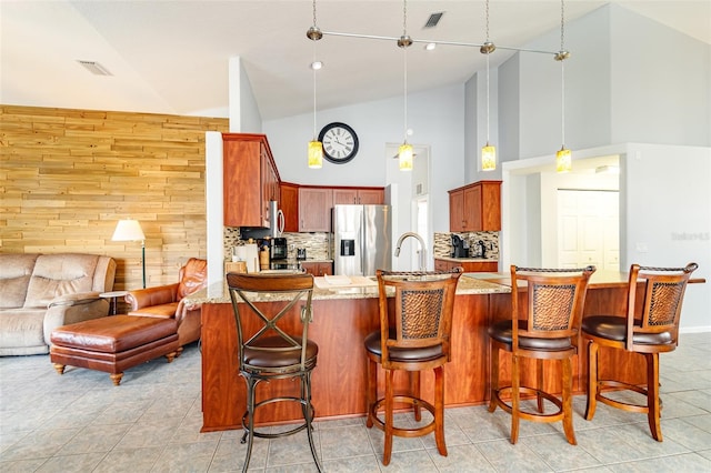 kitchen featuring stainless steel fridge with ice dispenser, high vaulted ceiling, light tile floors, a breakfast bar area, and pendant lighting