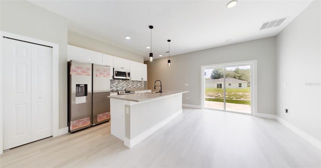 kitchen with stainless steel appliances, decorative light fixtures, tasteful backsplash, a center island with sink, and light wood-type flooring