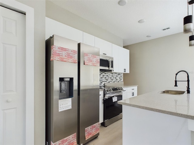 kitchen featuring appliances with stainless steel finishes, sink, light wood-type flooring, white cabinets, and tasteful backsplash