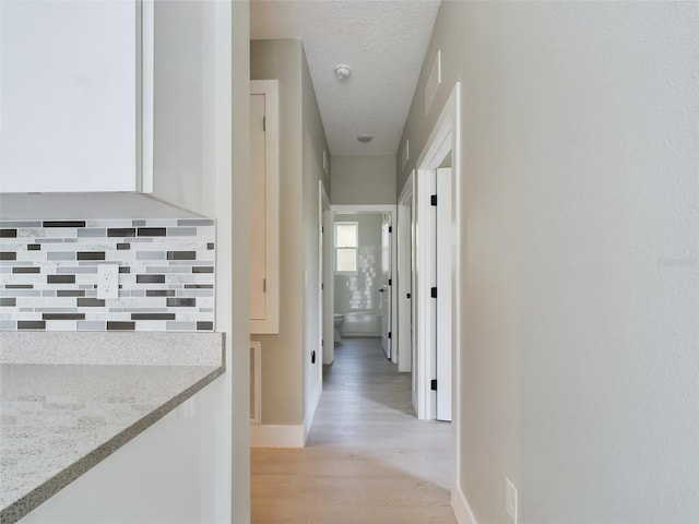 hall with a textured ceiling and light wood-type flooring