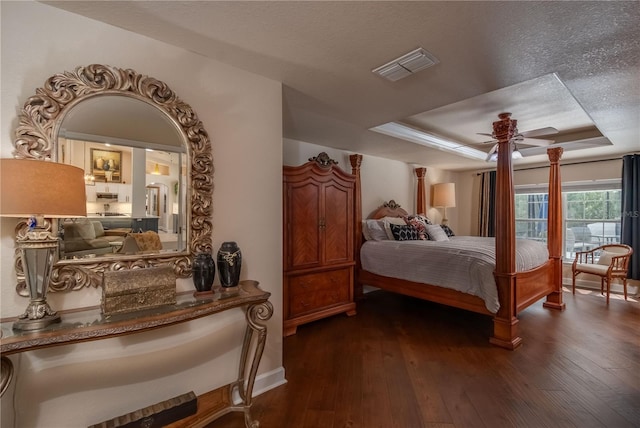 bedroom with a raised ceiling, ceiling fan, dark wood-type flooring, and a textured ceiling