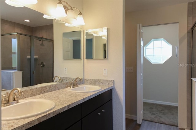 bathroom with a shower with shower door, double sink, vanity with extensive cabinet space, and hardwood / wood-style flooring