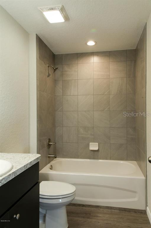 full bathroom featuring vanity, hardwood / wood-style floors, tiled shower / bath combo, a textured ceiling, and toilet