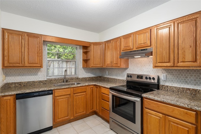 kitchen with light tile patterned floors, stainless steel appliances, dark stone countertops, a textured ceiling, and sink