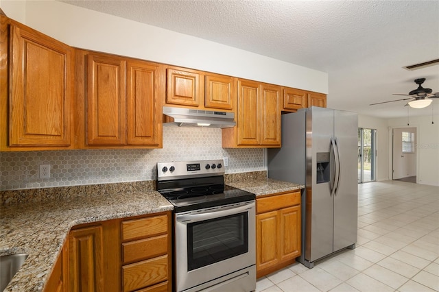 kitchen with a textured ceiling, appliances with stainless steel finishes, decorative backsplash, ceiling fan, and light stone counters