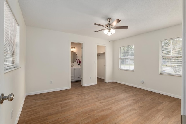 unfurnished bedroom featuring ensuite bath, a walk in closet, light hardwood / wood-style floors, a closet, and ceiling fan