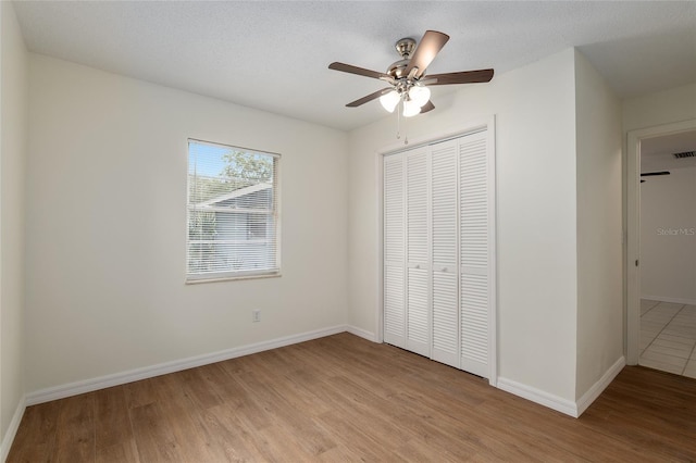 unfurnished bedroom with ceiling fan, a closet, a textured ceiling, and light hardwood / wood-style flooring