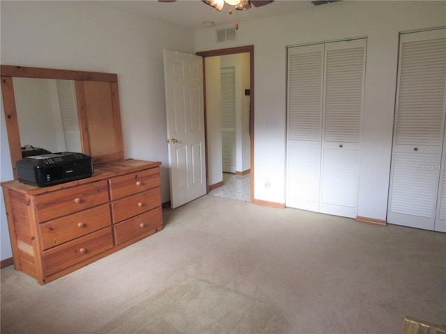 carpeted bedroom featuring ceiling fan and two closets