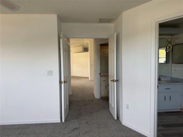 hallway with a textured ceiling and dark colored carpet