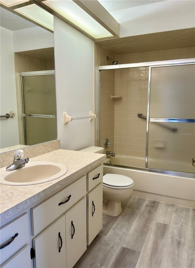 full bathroom featuring a textured ceiling, hardwood / wood-style flooring, shower / bath combination with glass door, toilet, and vanity