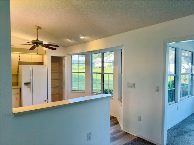 kitchen with ceiling fan, white fridge with ice dispenser, white cabinetry, a textured ceiling, and wood-type flooring