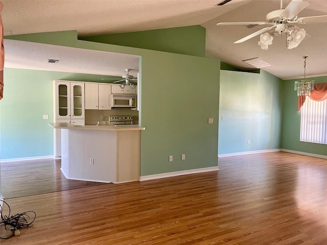 kitchen featuring hardwood / wood-style flooring, vaulted ceiling, ceiling fan with notable chandelier, white cabinets, and range