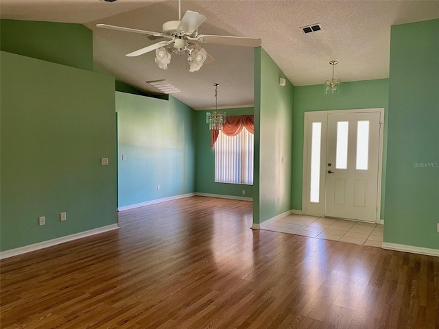 foyer entrance featuring lofted ceiling, ceiling fan with notable chandelier, a wealth of natural light, and light hardwood / wood-style flooring