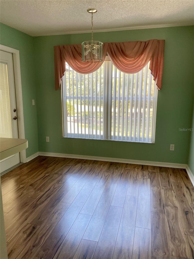 empty room with a chandelier, a textured ceiling, and dark hardwood / wood-style flooring