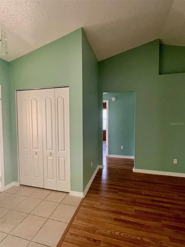 unfurnished bedroom featuring an inviting chandelier, light tile flooring, lofted ceiling, a closet, and a textured ceiling