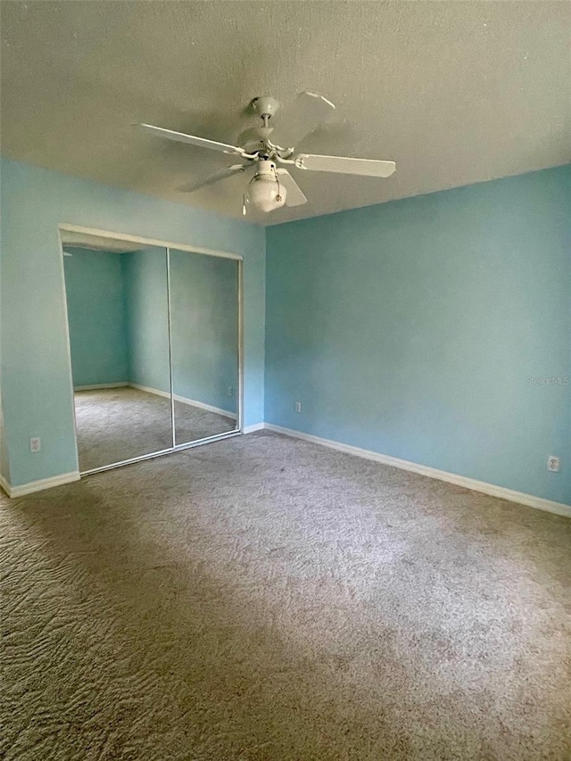 interior space with a closet, a textured ceiling, dark colored carpet, and ceiling fan