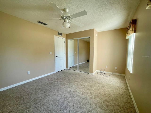 unfurnished bedroom featuring ceiling fan, a closet, light carpet, and a textured ceiling