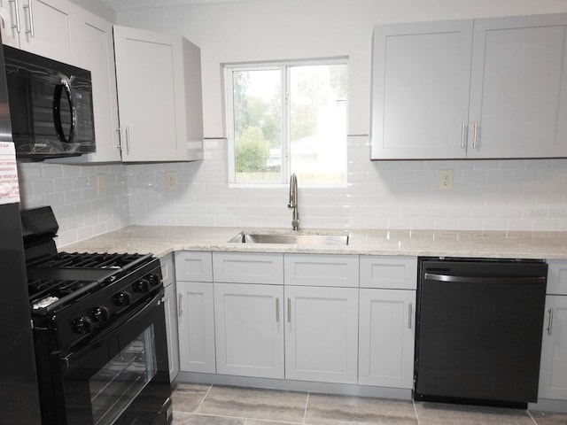 kitchen with sink, light tile floors, light stone countertops, black appliances, and tasteful backsplash