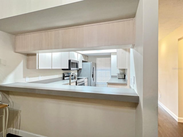 kitchen with kitchen peninsula, appliances with stainless steel finishes, light hardwood / wood-style flooring, light brown cabinets, and white cabinetry