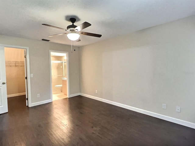 unfurnished bedroom with a closet, ceiling fan, dark wood-type flooring, ensuite bath, and a spacious closet