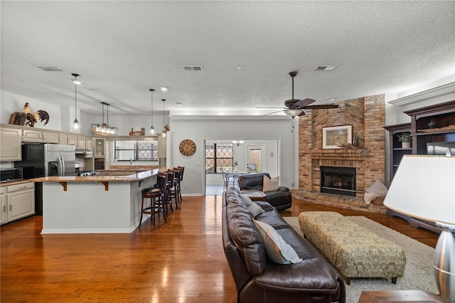 living room featuring brick wall, ceiling fan, hardwood / wood-style floors, a fireplace, and a textured ceiling