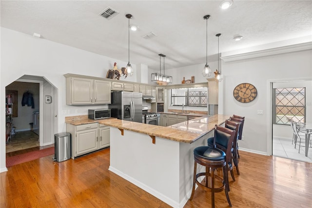 kitchen with pendant lighting, light hardwood / wood-style floors, appliances with stainless steel finishes, and a breakfast bar