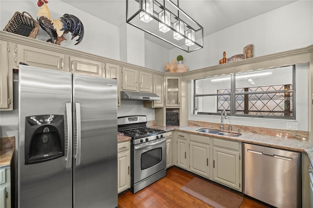 kitchen with appliances with stainless steel finishes, wood-type flooring, sink, light stone counters, and cream cabinets