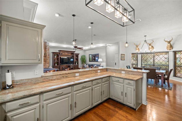 kitchen featuring an inviting chandelier, wood-type flooring, a textured ceiling, light stone counters, and pendant lighting