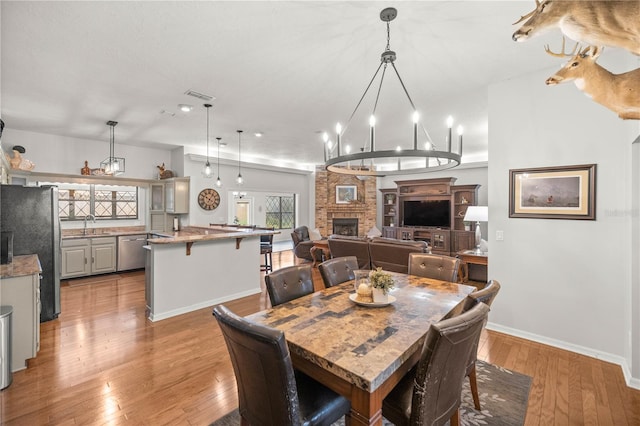 dining room with an inviting chandelier, sink, a stone fireplace, and light hardwood / wood-style flooring