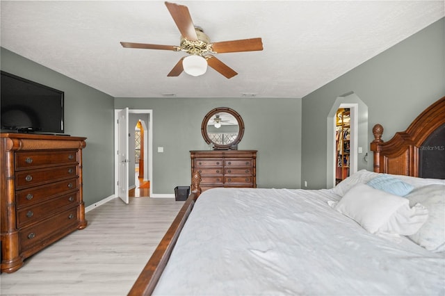 bedroom featuring light hardwood / wood-style floors, a walk in closet, ceiling fan, a textured ceiling, and a closet