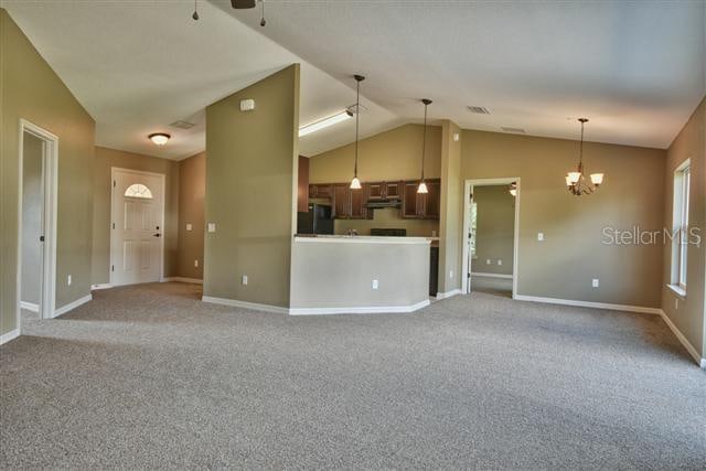 unfurnished living room with high vaulted ceiling, a chandelier, and carpet