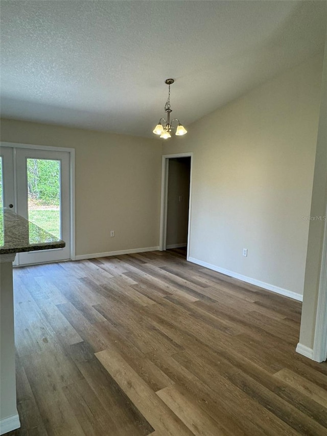 unfurnished room featuring hardwood / wood-style flooring, a textured ceiling, and a notable chandelier