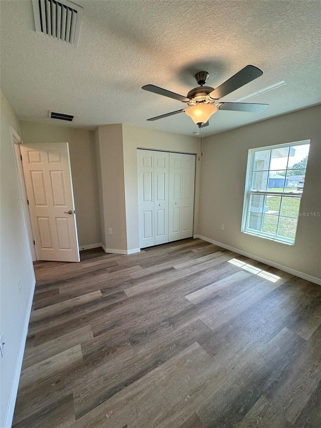 unfurnished bedroom with hardwood / wood-style flooring, a textured ceiling, ceiling fan, and a closet