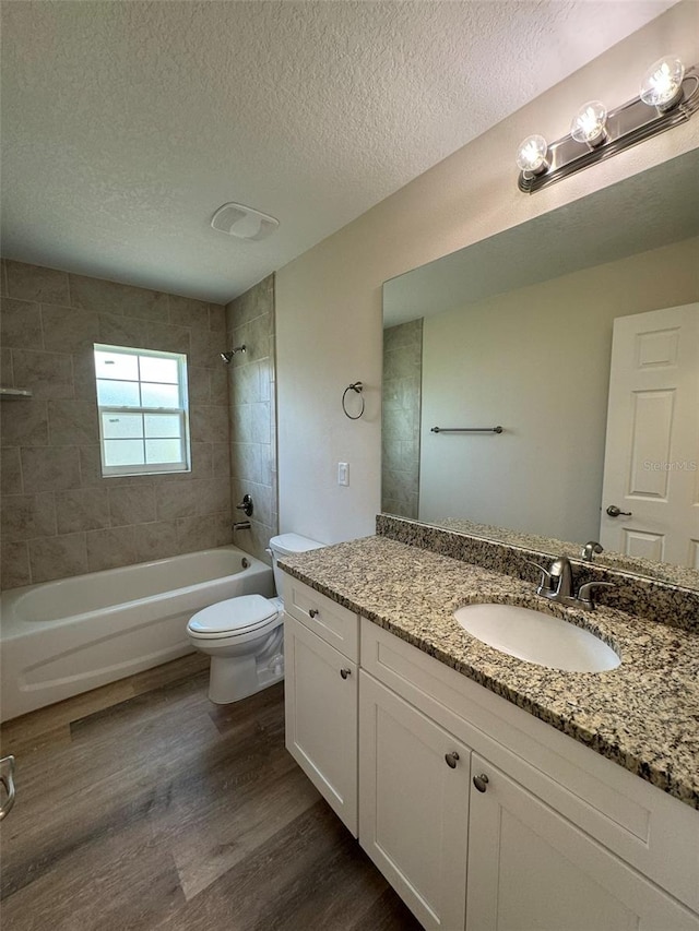 full bathroom with hardwood / wood-style floors, vanity, a textured ceiling, tiled shower / bath, and toilet