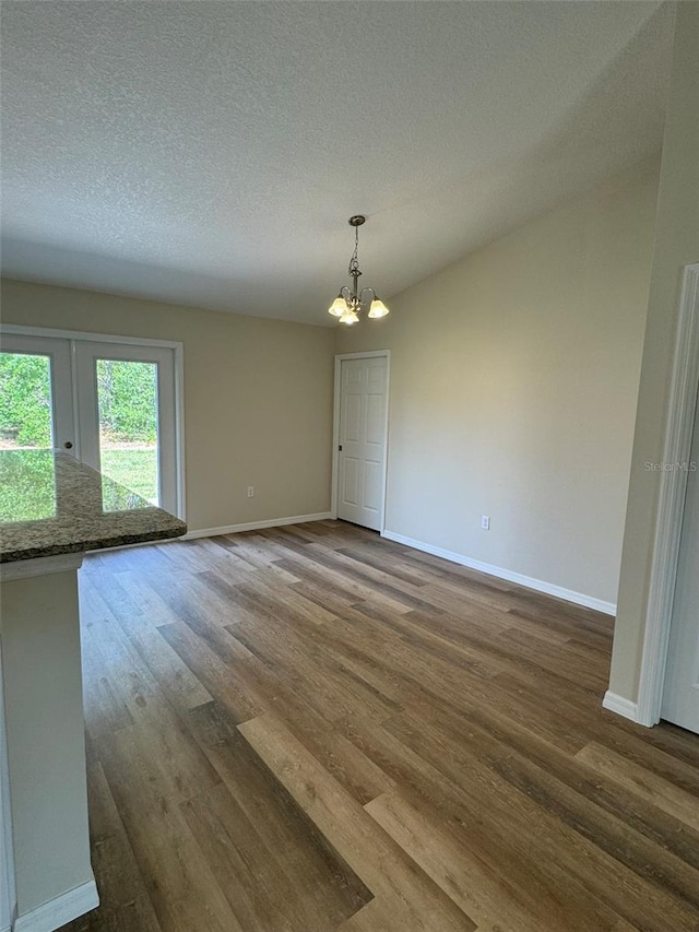 unfurnished dining area featuring dark hardwood / wood-style flooring, a textured ceiling, and a chandelier