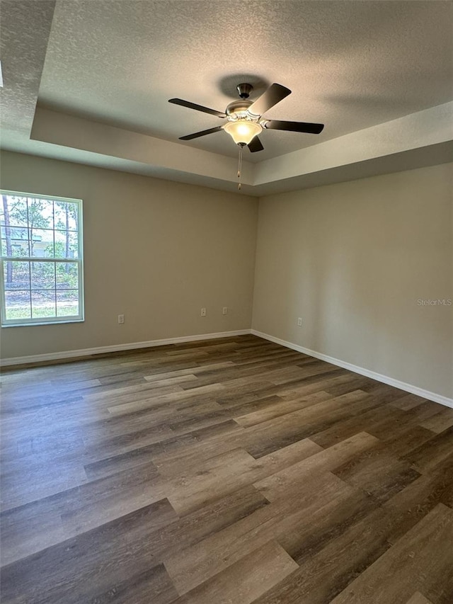 unfurnished room with ceiling fan, dark wood-type flooring, a raised ceiling, and a textured ceiling