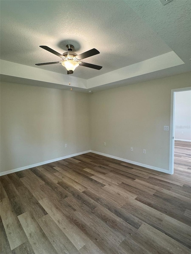 spare room with ceiling fan, a tray ceiling, dark hardwood / wood-style flooring, and a textured ceiling