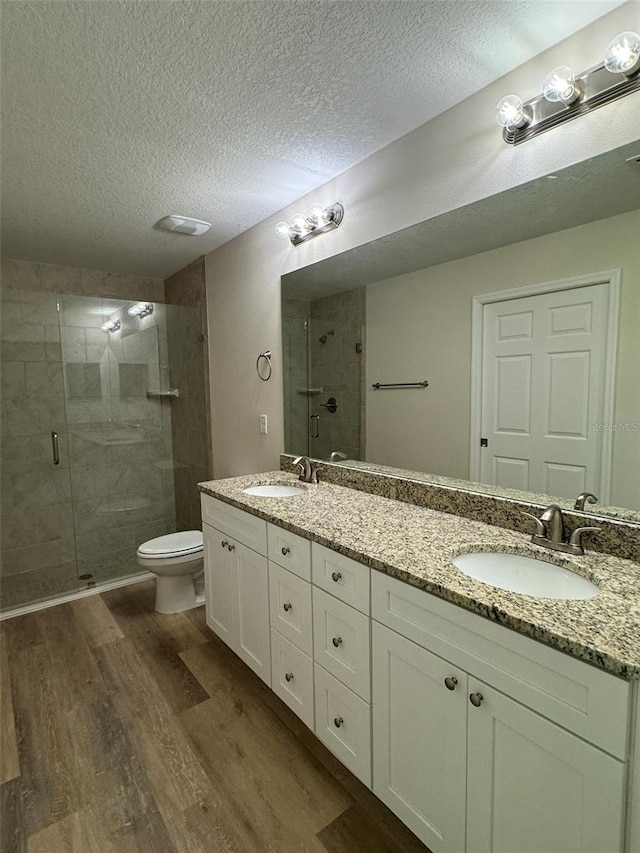 bathroom featuring hardwood / wood-style floors, vanity, a textured ceiling, a shower with shower door, and toilet