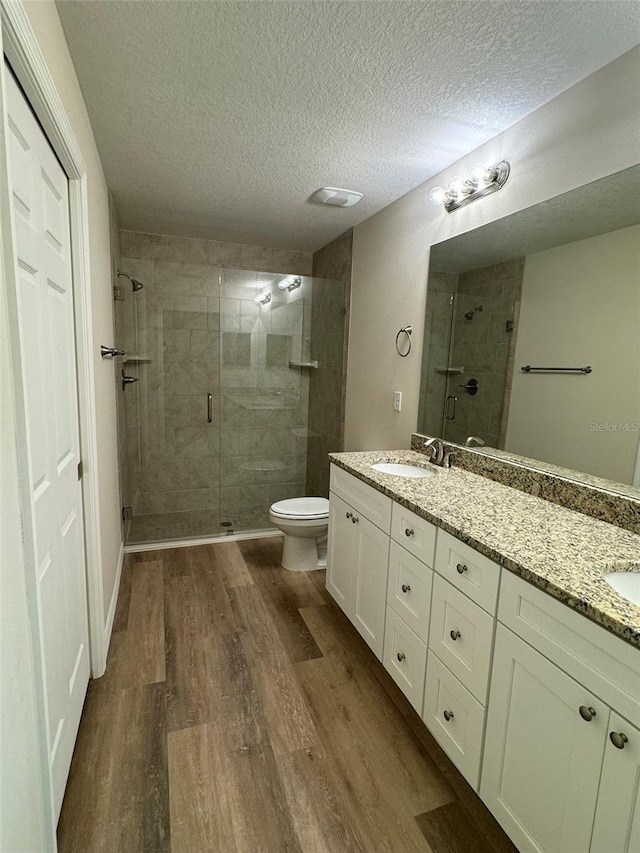 bathroom featuring hardwood / wood-style floors, vanity, a textured ceiling, a shower with shower door, and toilet