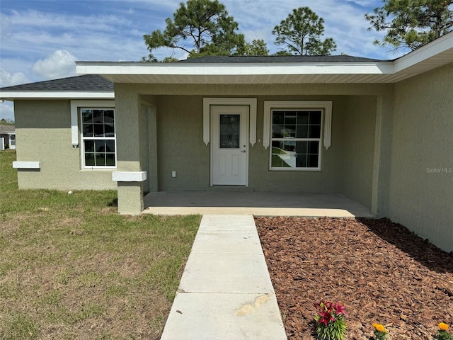 view of exterior entry featuring a patio and a lawn