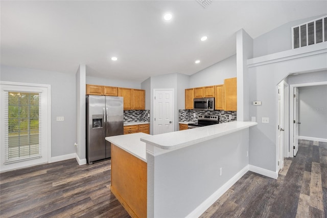 kitchen featuring kitchen peninsula, decorative backsplash, dark wood-type flooring, and appliances with stainless steel finishes