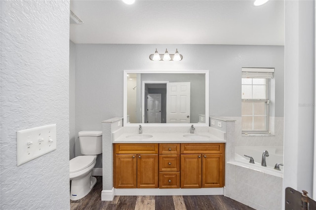 bathroom with hardwood / wood-style flooring, vanity, toilet, and tiled bath