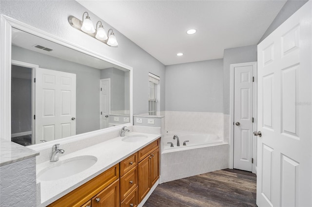 bathroom with vanity, a relaxing tiled tub, and wood-type flooring