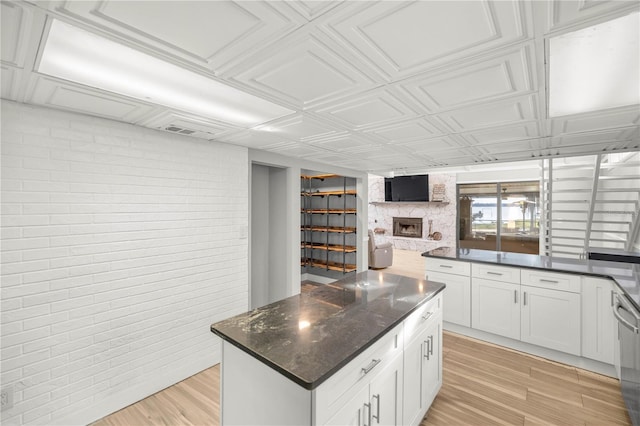 kitchen with white cabinets, brick wall, light wood-type flooring, and a stone fireplace